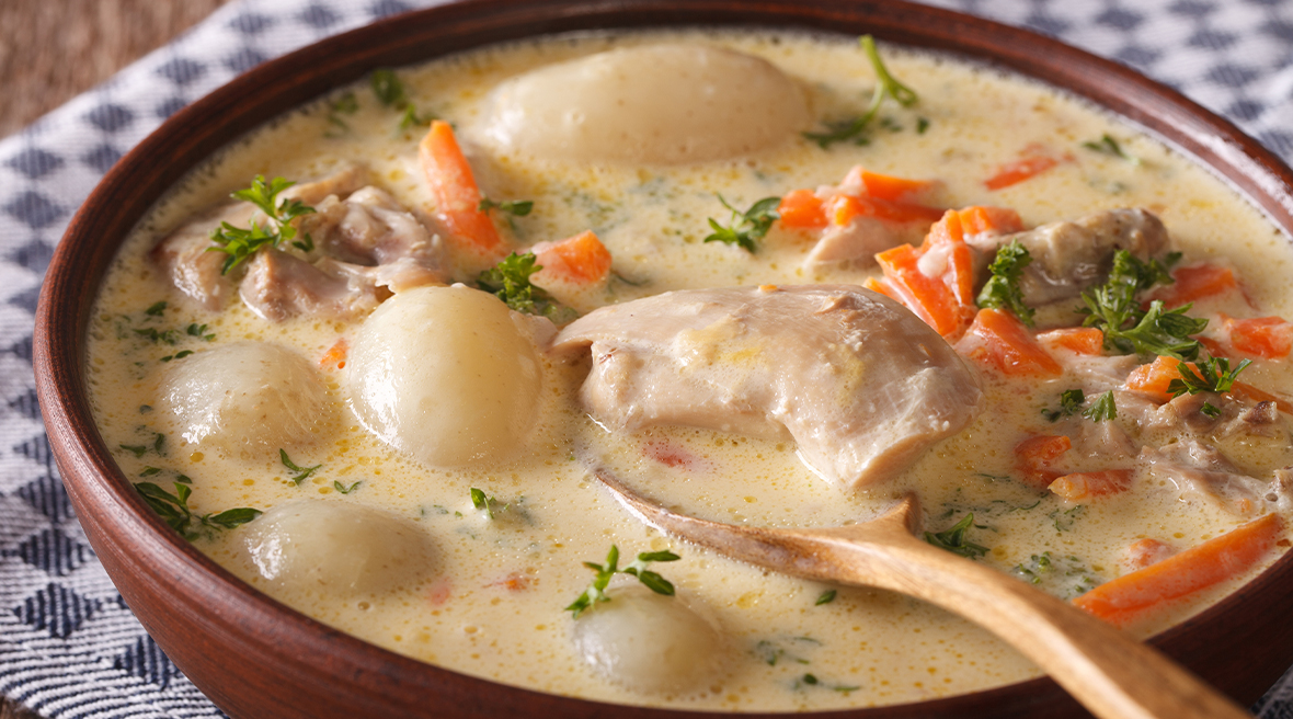 Traditional wooden bowl of creamy stew with carrots and chicken with a wooden spoon inside